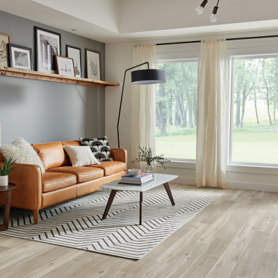 Bright living room with a tan sofa, black-and-white throw pillows, framed photos on the wall, a patterned area rug, a white coffee table, a floor lamp, and large windows 